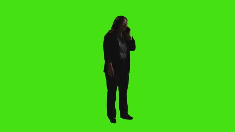 businesswoman sending or reading text message or scrolling online on mobile phone standing against green screen with low key lighting