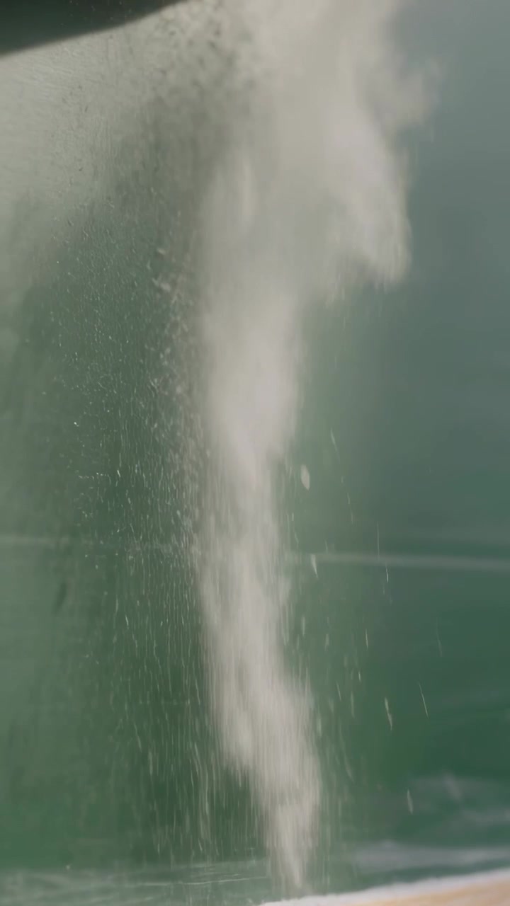Video verticale: Colonna di nebbia che fuoriesce e cade da una sporgenza, crescendo e poi svanendo su una giuntura di parete verde.