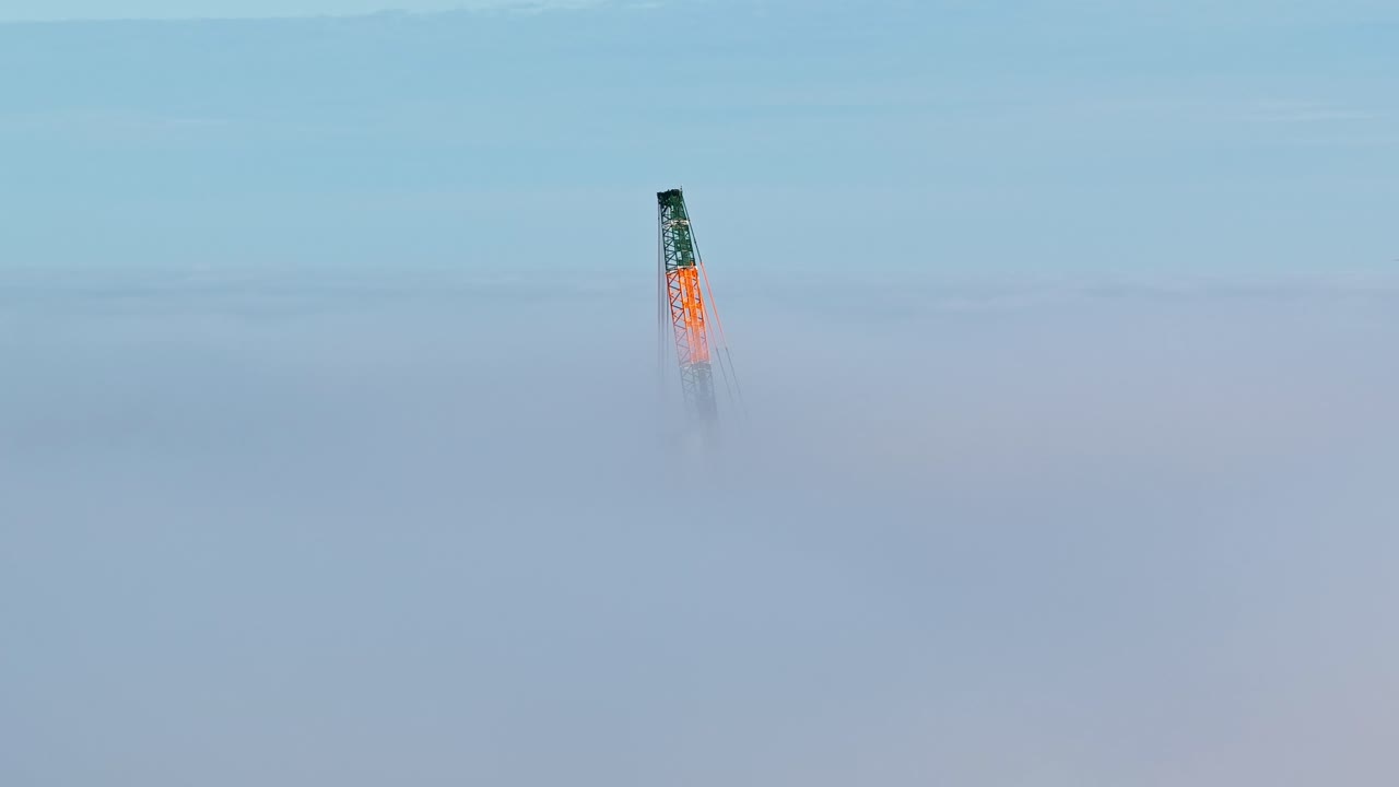 Intriguing aerial view of a crane top piercing through the thick clouds