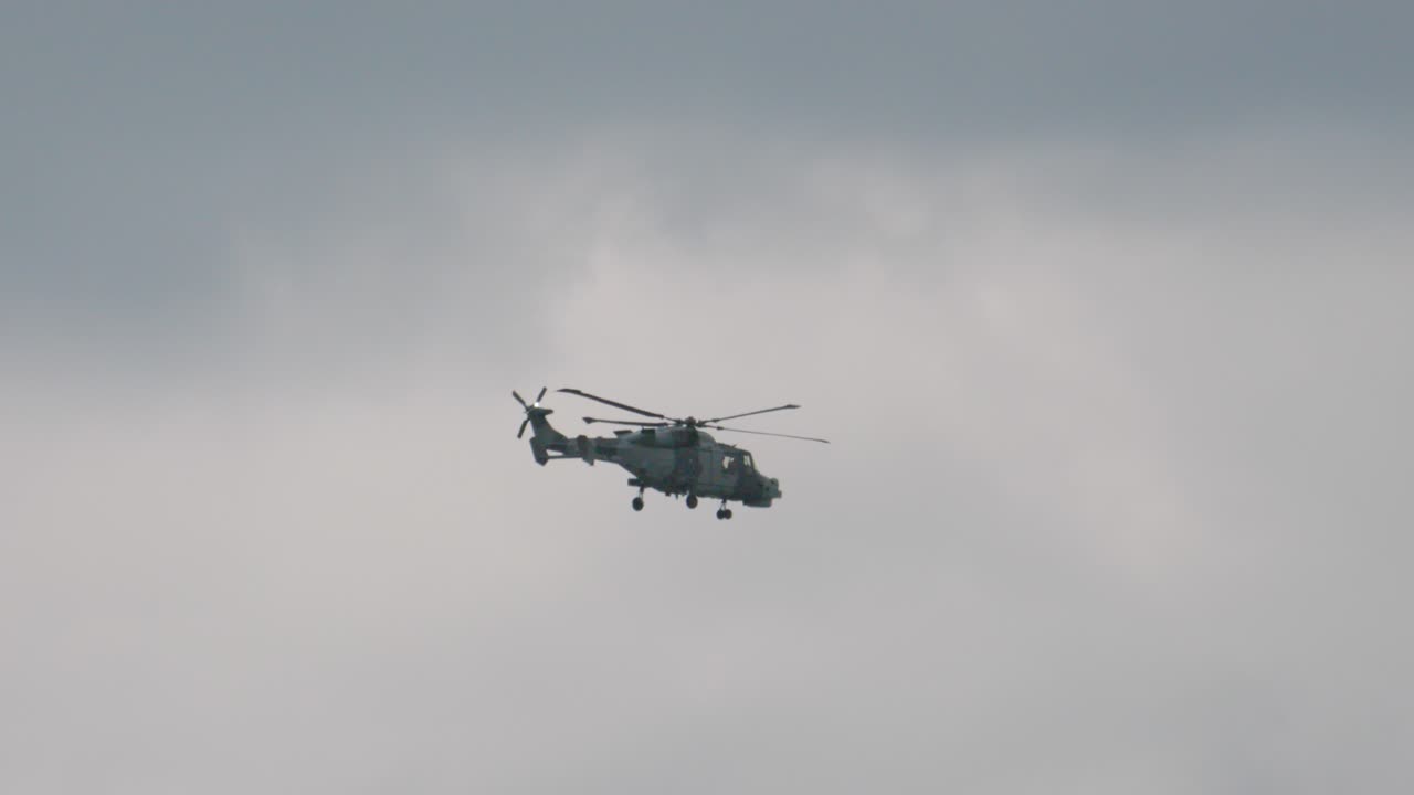 Wildcat Helicopter Travelling Left to Right with Rapid Rotors Turning Against Overcast Sky Background. British Chopper Used in Navy for Military Purposes Capable of Vertical Takeoff. Aviation Footage