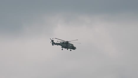 wildcat helicopter travelling left to right with rapid rotors turning against overcast sky background. british chopper used in navy for military purposes capable of vertical takeoff. aviation footage