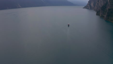 Slow-tilt-up-aerial-shot-of-a-large-boat-traveling-on-the-famous-Garda-Lake,-Lombardy,-Italy