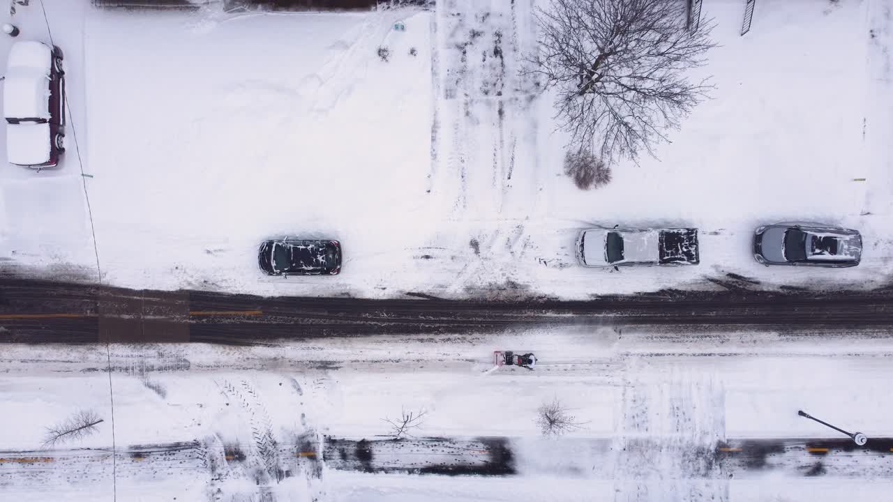 Drone top down descends on person pushing snow blower in a snow covered street in Quebec, Canada