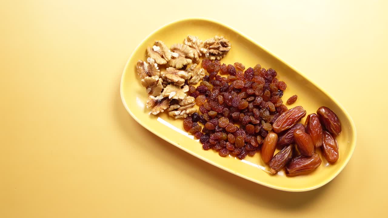 Close up of walnuts, dates and raisins on a yellow plate.