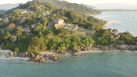 Aerial-drone-view-establishing-shot-of-famous-landmark-brazilian-fortress-at-sunset,-Fortaleza-Sao-Jose-Da-Ponta-Grossa,-Jurere-Internacional,-Florianopolis,-Santa-Catarina,-Brazil