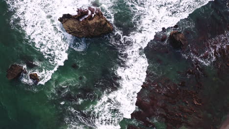 White-capped-foamy-sea-waves-washing-upon-sharp-jagged-rocks-on-coast