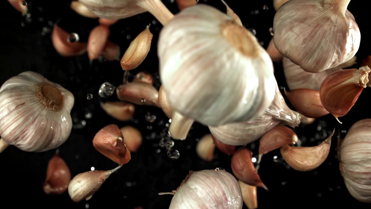 Bulbi e spicchi d'aglio freschi che cadono con schizzi d'acqua al rallentatore.