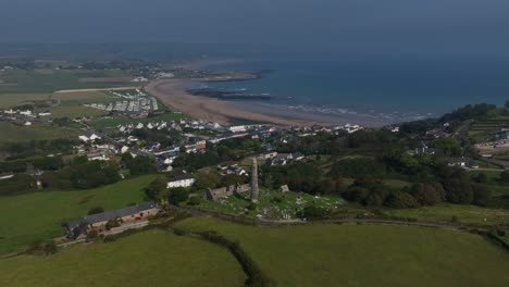 st. declan's monastery, ardmore, county waterford, ireland, september 2024. drone ascends in a panoramic counter clockwise orbit high above round tower and graveyard as a road winds toward the coast.
