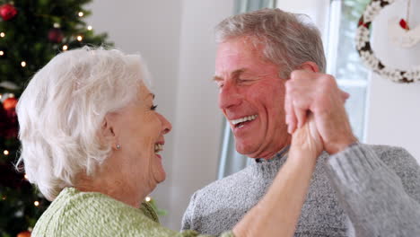 Cerca-De-Una-Romántica-Pareja-De-Ancianos-Bailando-Juntos-En-Casa-Con-Un-árbol-De-Navidad-En-El-Fondo