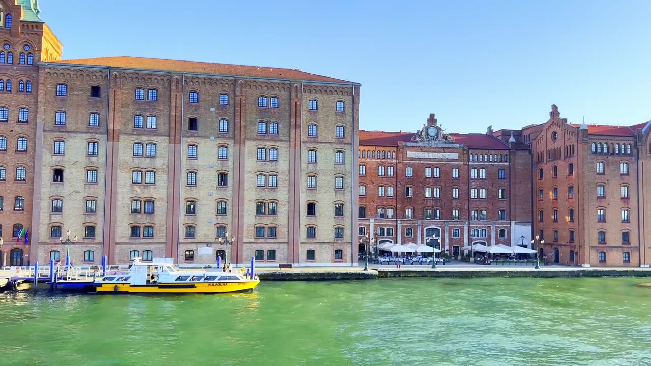 Filmato di viaggio che mostra l'edificio dell'Hotel Molino Stucky e l'architettura circostante sul lungomare, ripreso da una barca in movimento a Venezia, Italia