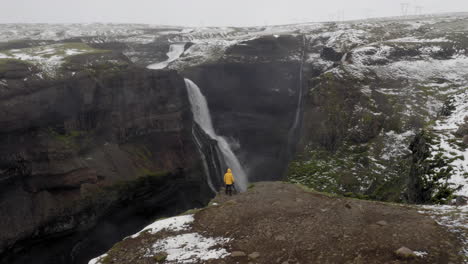 Aerial:-Slow-panning-shot-of-a-man-standing-near-the-edge-of-a-cliff,-between-Haifoss-and-Granni-waterfalls-in-Iceland