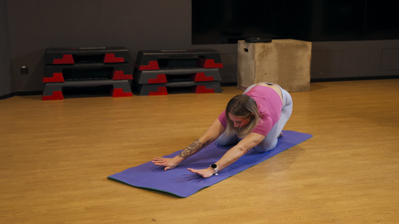 Fitness enthusiast stretching on a mat in a gym, performing a deep lunge pose to improve flexibility and mobility, swaying and leaning back into hips