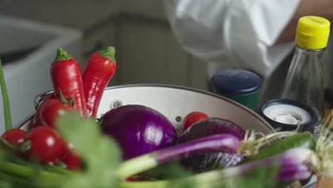 chef hand picks up cucumber from bowl with vegetables on a kitchen table