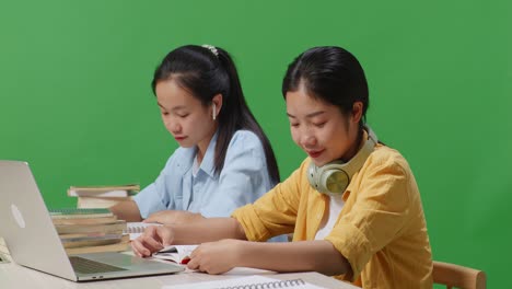 close up of asian woman students smiling and waving hands while sitting on a table with laptop in the green screen background classroom