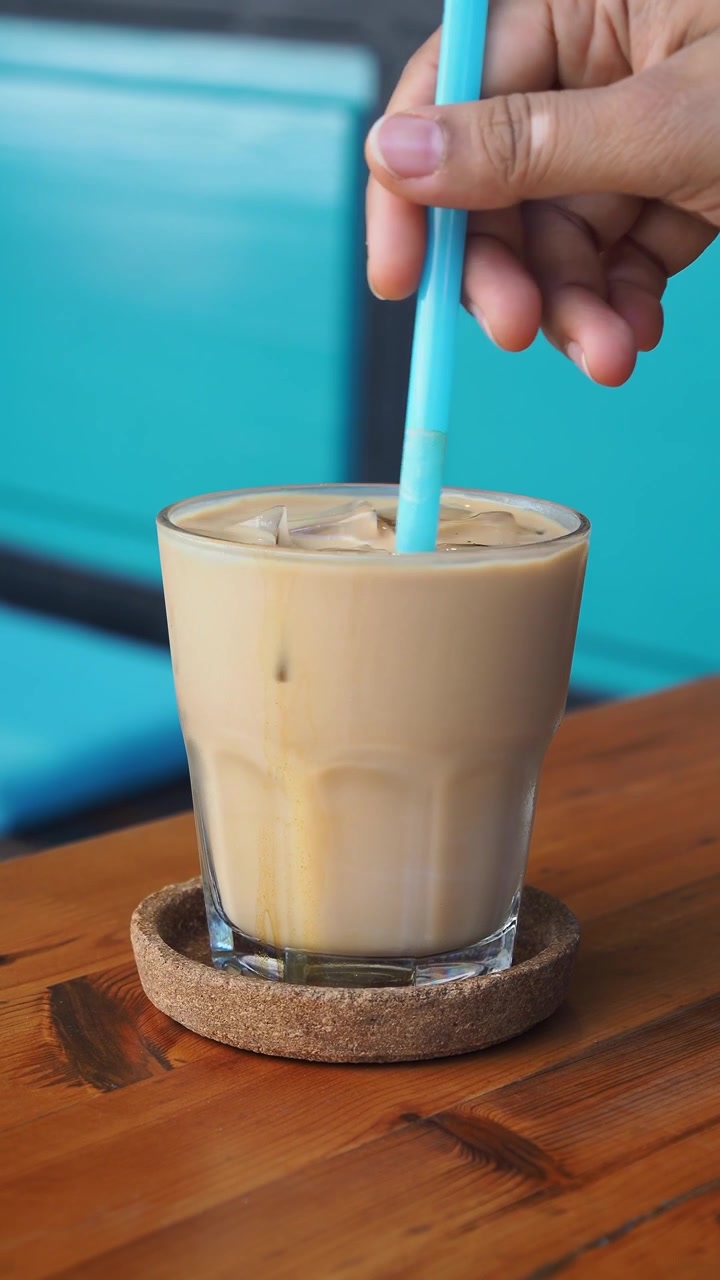 Mano che mescola caffè freddo con una cannuccia blu