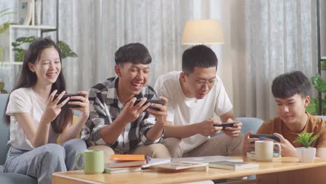 asian teen group playing game on smartphone, break time after working on online project, students with books and laptop studying at home