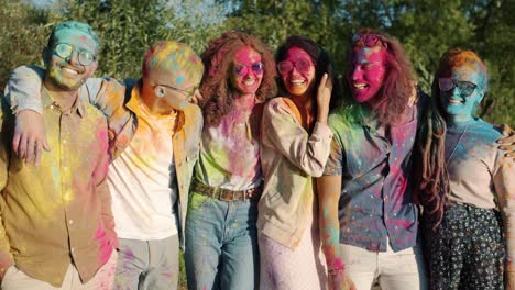 portrait of happy friends with colorful faces hair and clothes standing outdoors and smiling during holi festival