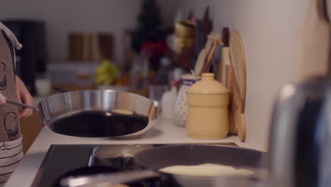 woman frying pancakes in pan in kitchen