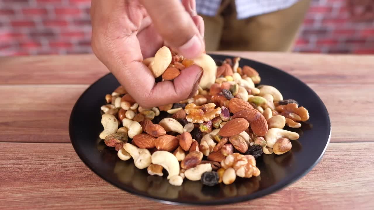 Person Picking Cashews from a Plate of Mixed Nuts