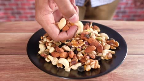 Person Picking Cashews from a Plate of Mixed Nuts