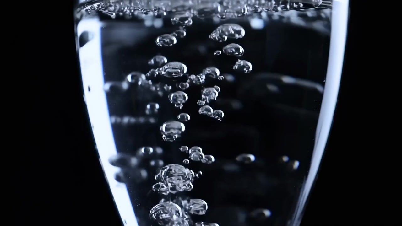 Densa colonna verticale di bolle d'aria all'interno di un bicchiere d'acqua trasparente, catturata in un primo piano frontale ravvicinato su sfondo nero, con bolle che variano da piccole sfere a quelle più grandi e coalesce.