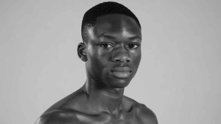 Reaccionando a la señal de la cámara, modelo sin camiseta girando la cabeza y ajustando la mirada en un estudio, con fondo gris.