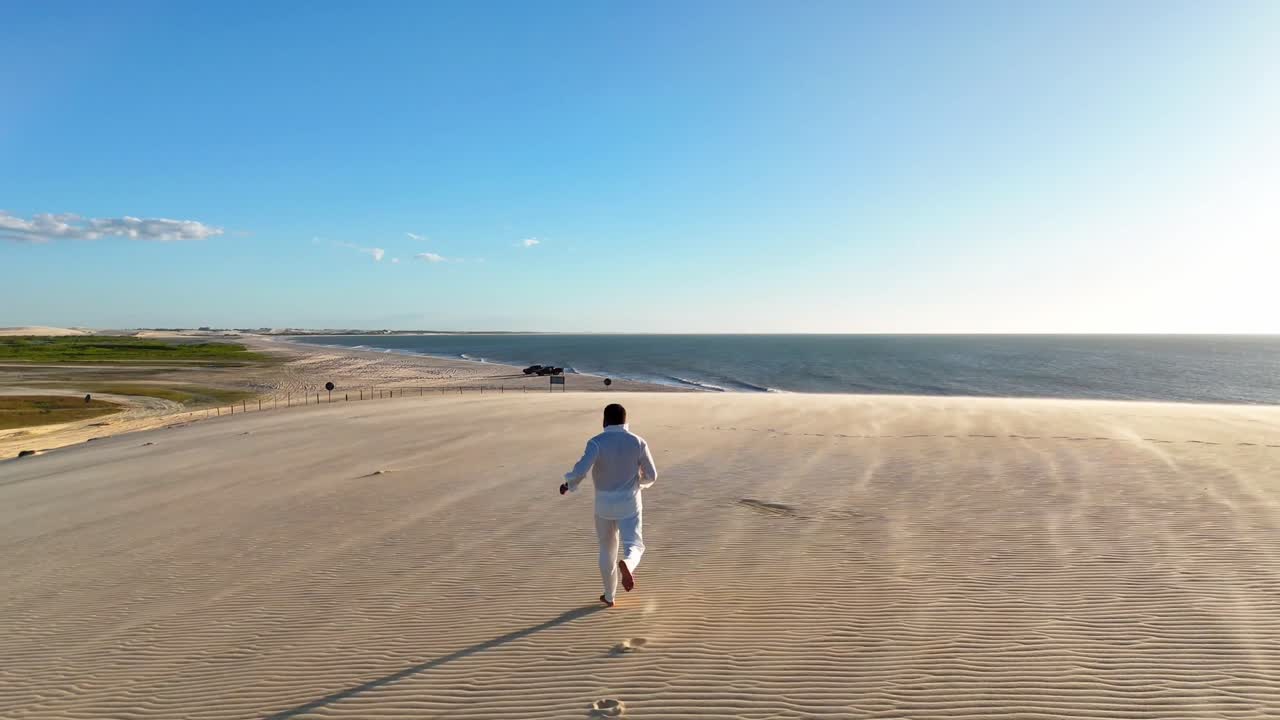 man dressed in soft clothing running through the dunes of Jericoacoara