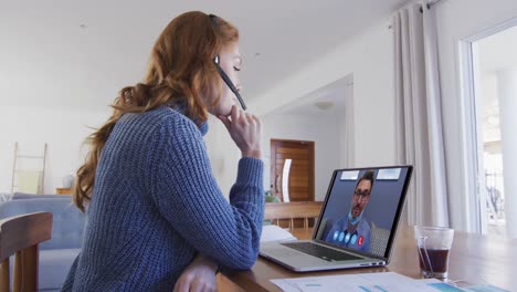 caucasian woman using laptop and phone headset on video call with male colleague