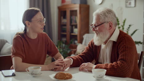 young woman holding hand of elderly grandfather during conversation at home