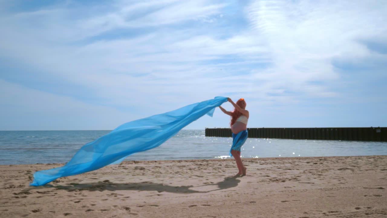 바람에 날아다니는 파란색 옷으로 재미를 느끼는 임산부 해변