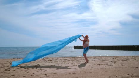 Pregnant-woman-having-fun-with-blue-cloth-flying-in-wind.-Pregnant-woman-beach