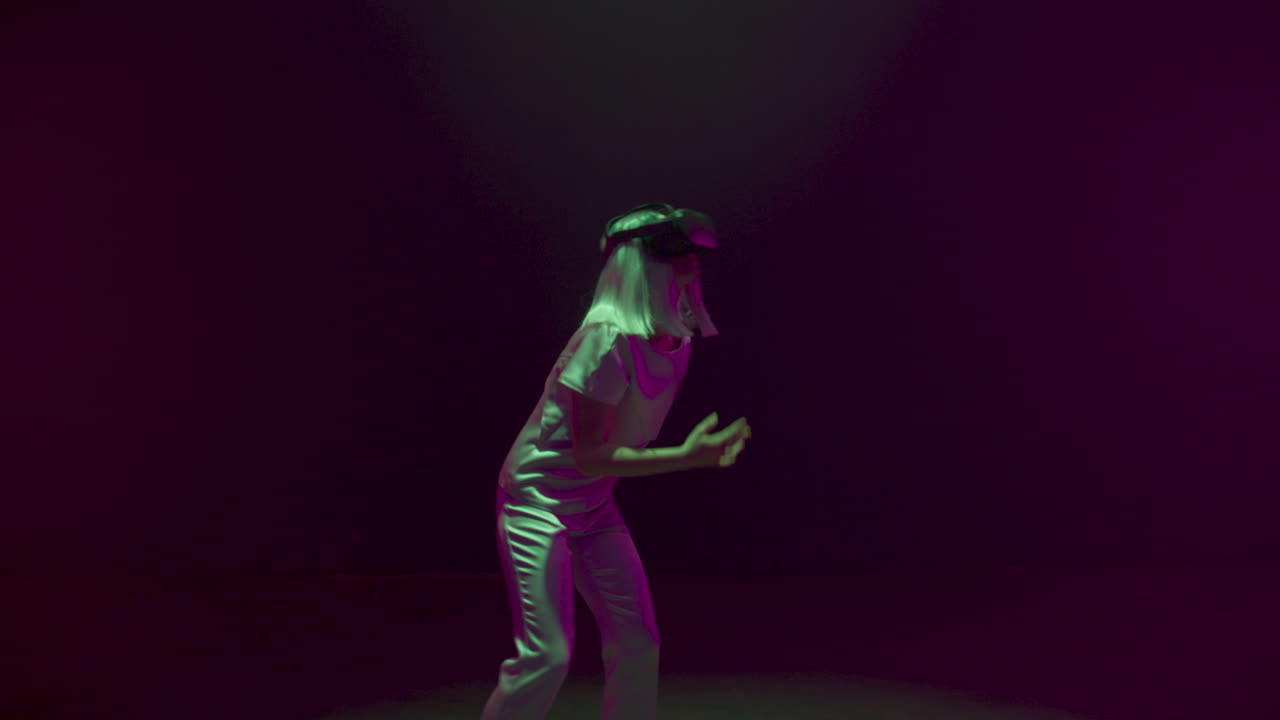 Ragazza felice che balla con visore VR sotto luci al neon. Millennial futuristico che si diverte.