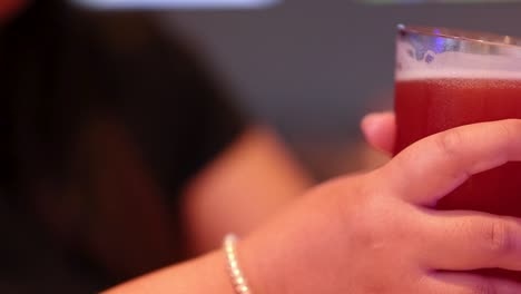 a hand with a bracelet holds a glass of red beverage, showcasing a casual moment.