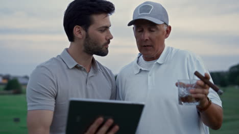 Dos-Golfistas-Navegando-Por-La-Tableta-En-El-Campo.-Hombres-Ricos-Que-Utilizan-La-Tecnología-En-Línea.