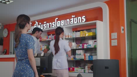 asian female pharmacist selling prescription medicine to customers.