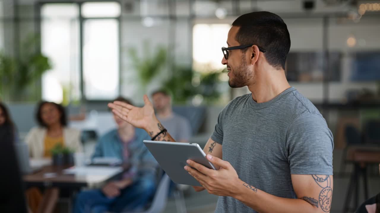 Tapping tablet, presenter in gray tee leading team discussion at open-plan office meeting