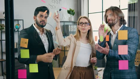 el equipo creativo experimentado está satisfecho con los resultados del trabajo conjunto en un nuevo proyecto y aplaudiendo mirando dibujos en la pared de vidrio de la oficina