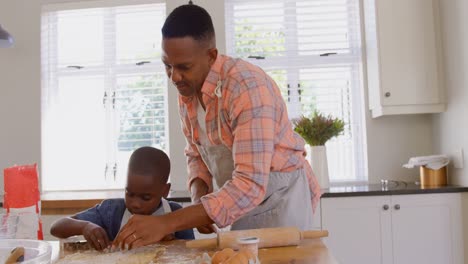 Front-view-of-mid-adult-black-father-and-son-baking-cookies-in-kitchen-of-comfortable-home-4k