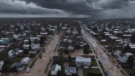 dramática vista aérea que revela vecindarios residenciales inundados con agua fangosa, calles y propiedades abrumadoras bajo un cielo oscuro y ominoso durante eventos climáticos extremos