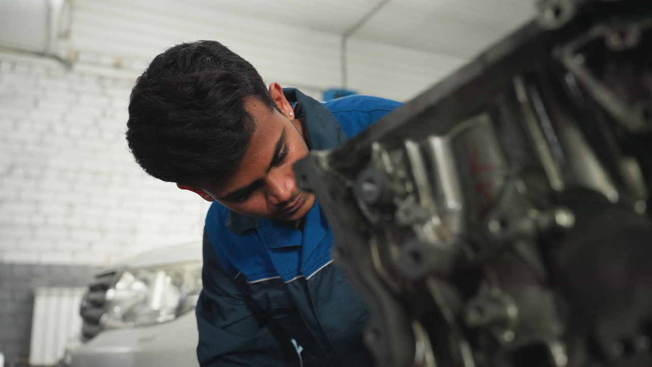 ingeniero que trabaja diligentemente en el bloque del motor en el taller de automóviles, centrándose en la reparación y inspección detalladas, con un claro énfasis en el trabajo mecánico y las herramientas
