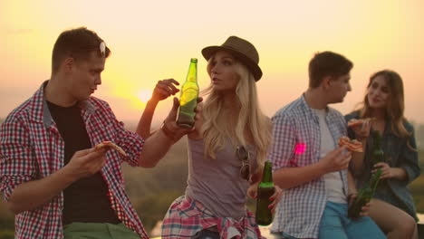 a loving couple on the roof drinks beer and enjoying the sunset. the girl in the hat gently strokes the head of her young man.