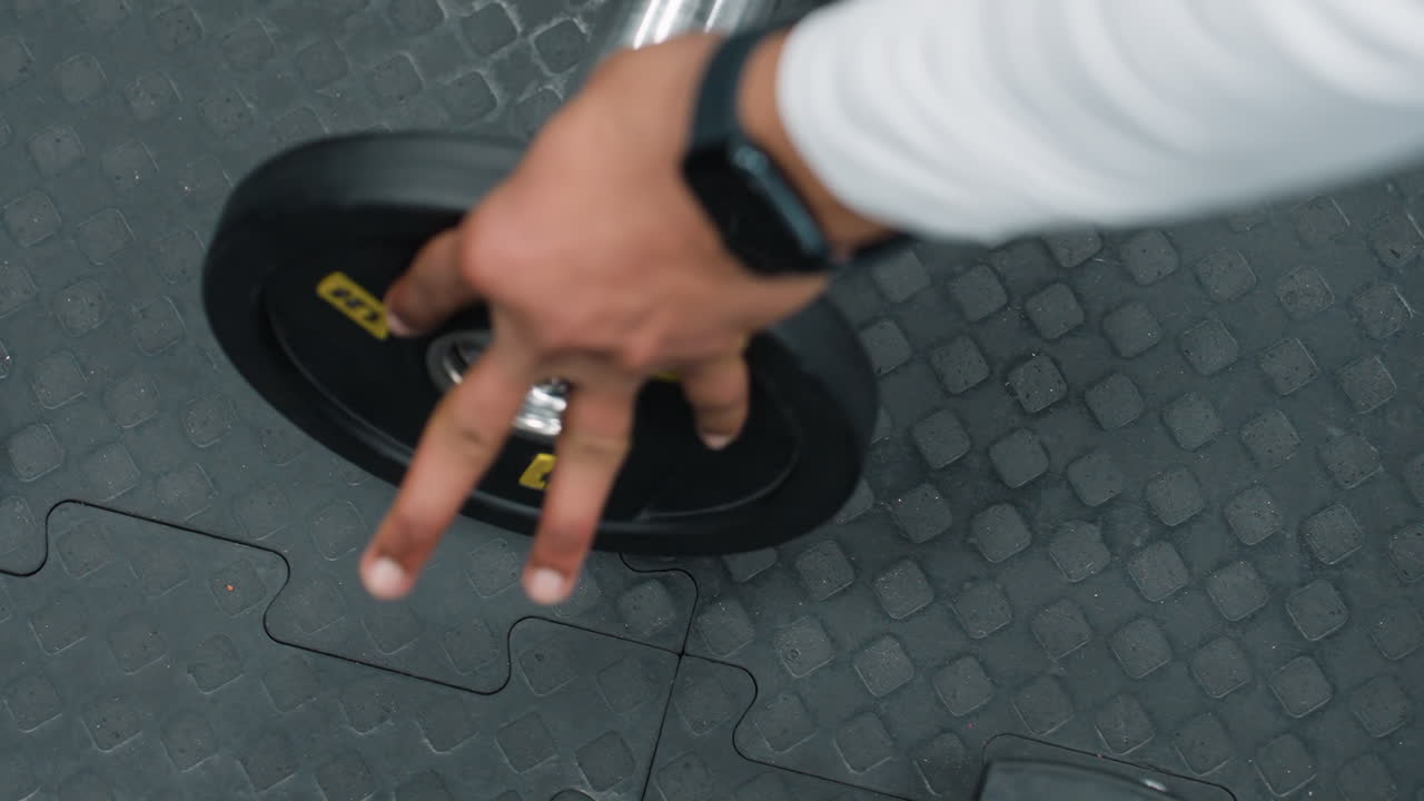 Top down close up of barbell beside 1.25 weight plate on black rubber gym flooring as person prepares to load bar for workout, showing details of chrome bar end and exercise preparation
