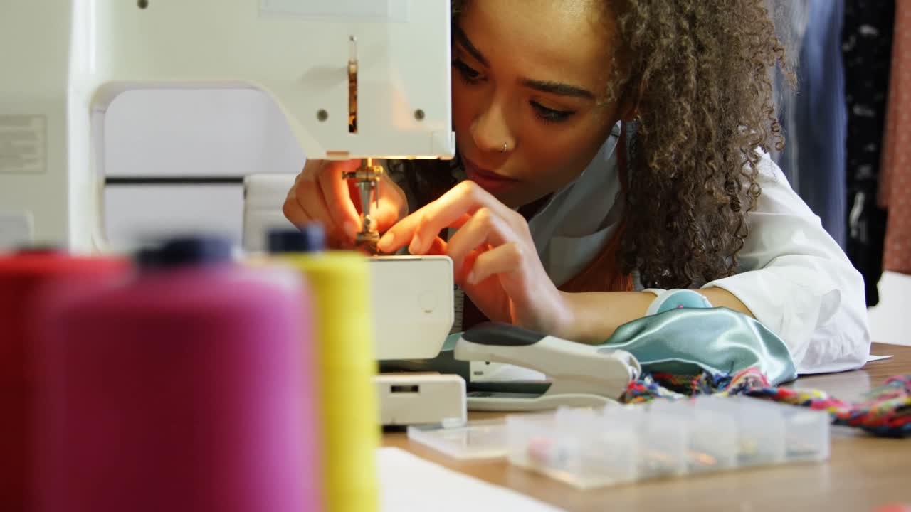 vista frontal de una diseñadora de moda afroamericana trabajando con una máquina de coser en un taller 4k