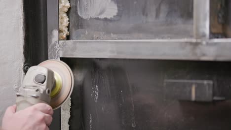 limpieza manual caucásica de costuras soldadas con una molienda angular con un disco de flap en la construcción metálica soldada de primer plano con largos rastros de chispas, cámara lenta