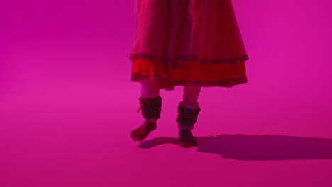 cerca de los pies y las campanas de la bailarina de kathak femenina realizando una danza vestida con el vestido tradicional indio contra un fondo púrpura