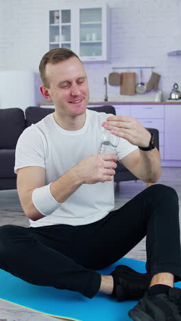 handsome young sportsman doing exercises on quarantine. lively athletic active man using his laptop and drinking water while training indoors vertical video