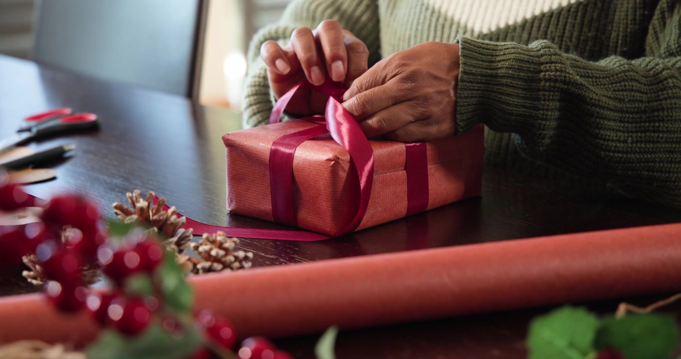 Con un nastro posato sulla scatola, le mani stanno allineando, piegando e annodando un fiocco per le festività.