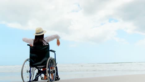 rear view of disabled woman sitting with arms up on wheelchair at beach 4k