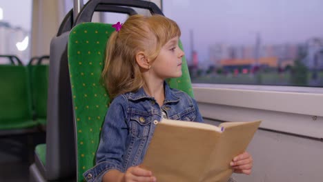 Portrait-of-attractive-little-child-girl-kid-sitting-at-empty-subway-train,-reading-interesting-book