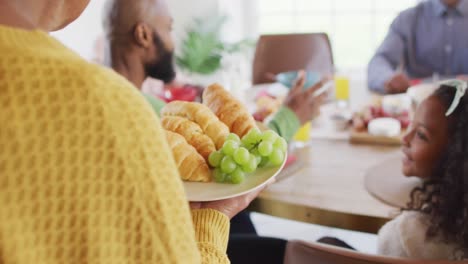 Video-of-happy-african-american-parents,-daughter-and-grandparents-serving-food-and-sitting-at-table